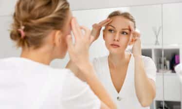 woman looks at forehead in mirror